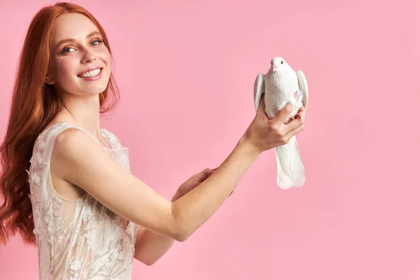 Redhaired caucasian woman holding white pigeon isolated over pink background — Stock Photo, Image