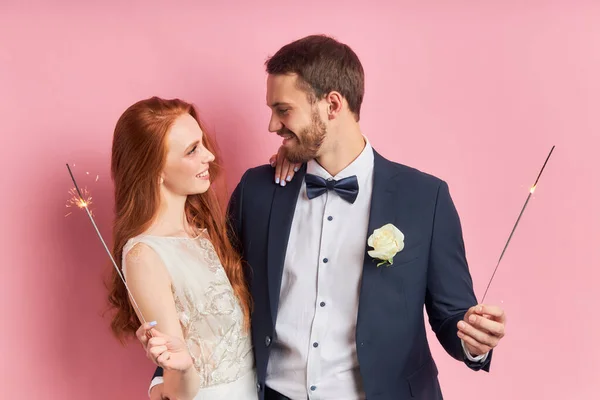 Beautiful young couple in love holding sparklers isolated over pink background — ストック写真