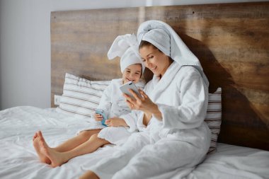 Kızı olan beyaz bir anne akıllı telefon kullanıyor.
