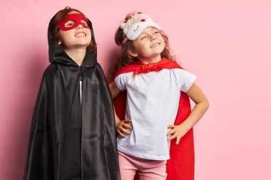 İki küçük süper kahraman pembe arka planda izole edilmiş bir şekilde yukarı bakıyor.