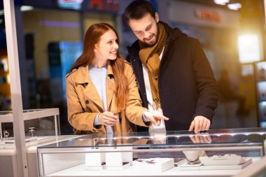 Kızıl saçlı bir kadın ve bir erkek kuyumcudan pahalı mücevherler seçiyor.