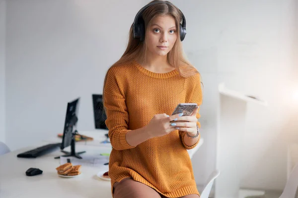 Zamyšlená mladá běloška držící smartphone v kanceláři — Stock fotografie