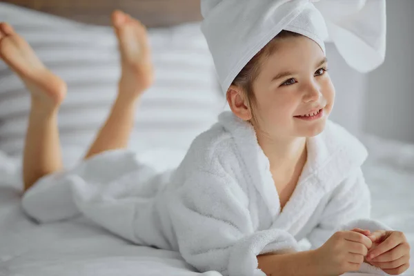 Chica hermosa caucásica en albornoz y toalla acostado en la cama y sonrisa —  Fotos de Stock