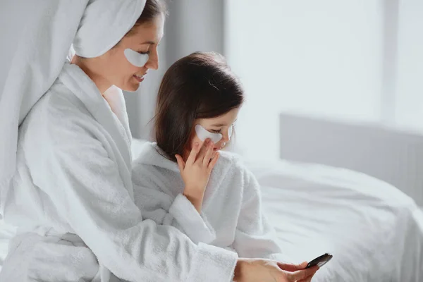 Geweldig Moeder en dochter zitten samen op bed in schoonheid maskers patches thuis — Stockfoto