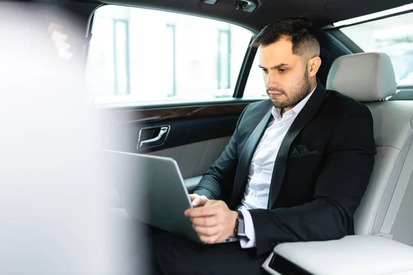 Attraktiver Mann sitzt in Luxuslimousine oder Auto und arbeitet am Laptop — Stockfoto