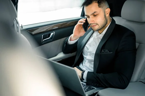 Kellemes magabiztos férfi szmokingban beszél telefonon Executive autóban — Stock Fotó