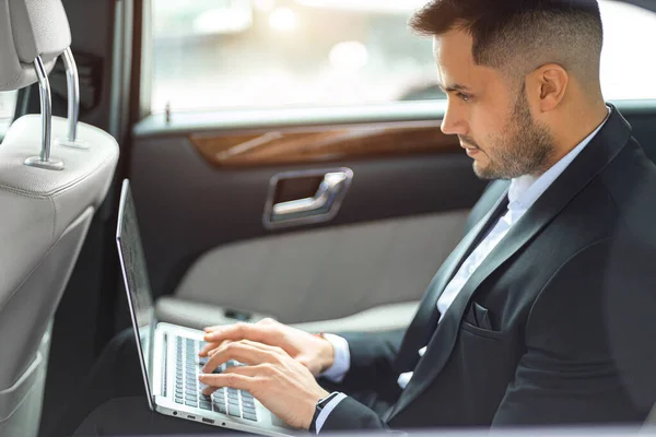 Male in formal wear with laptop in luxurious car