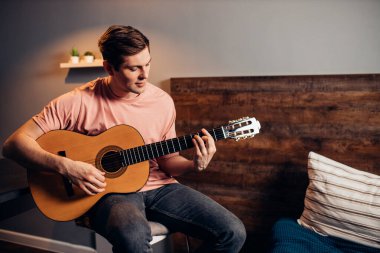 Gündelik gömlekli gitarist yatakta gitar çalıyor.