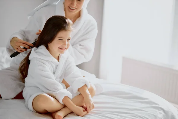 Sonriente familia amigable de madre e hija peinando el pelo en la cama —  Fotos de Stock