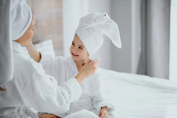 Atractiva mujer sentarse con hija sosteniendo cepillos para el maquillaje — Foto de Stock