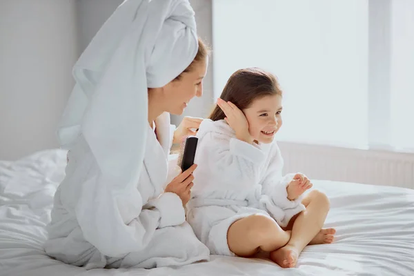 Mujer caucásica peinar pelo a la pequeña hija en la cama —  Fotos de Stock