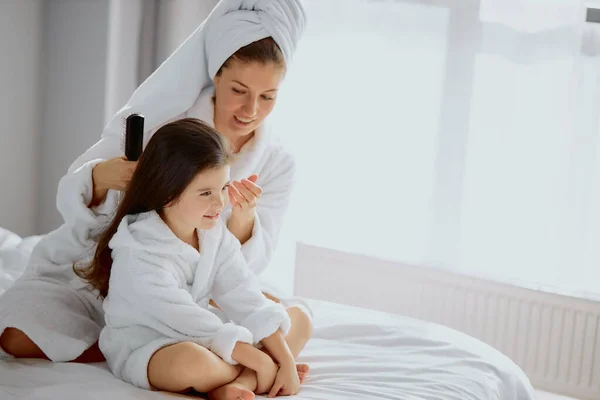 Caucasian woman comb hair to little daughter on bed — Stock Photo, Image