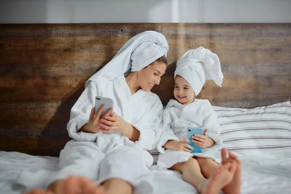 Adorable madre e hija usando teléfono inteligente en la cama en casa — Foto de Stock