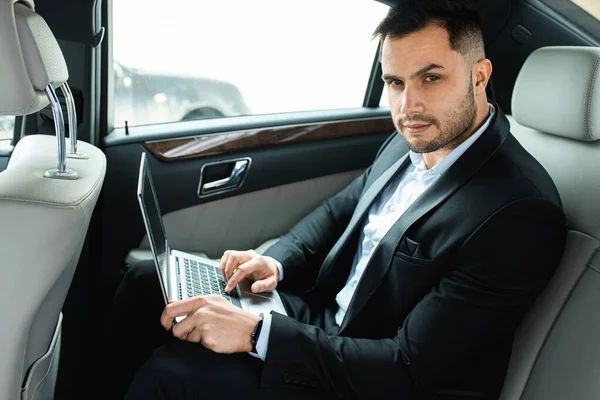 Schöner Mann in formeller Kleidung mit Laptop im luxuriösen Auto — Stockfoto