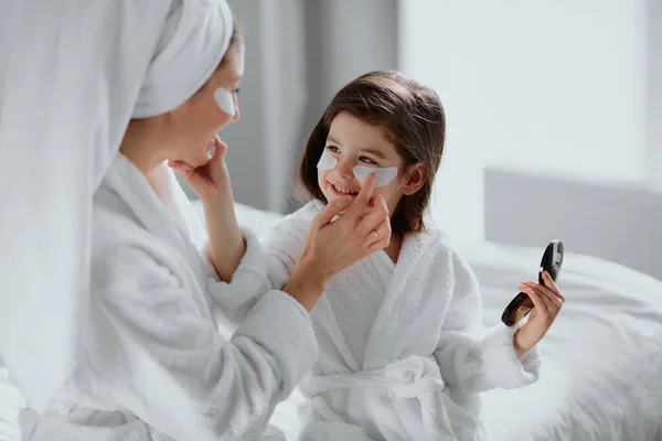 Słodkie matka i córka siedzieć razem na łóżku w piękno maski łatki w domu — Zdjęcie stockowe