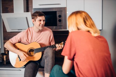 Kafkasyalı genç kadın ve erkek birlikte oturup gitar çalarlar.