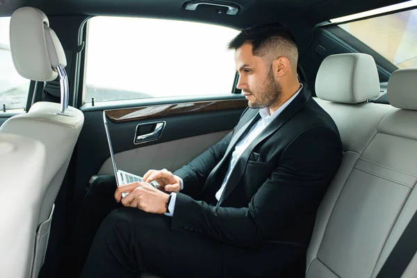 Vonzó férfi ül luxus limuzin vagy autó, dolgozik laptop számítógép — Stock Fotó