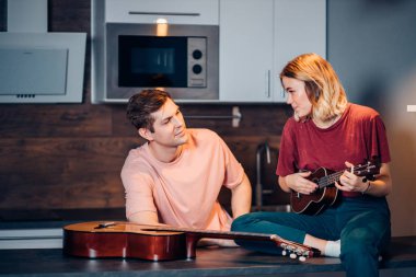 Genç bayan evde ukulele oynuyor.