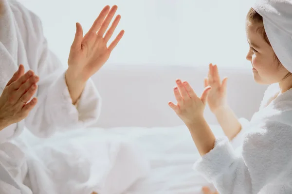 little girl playing clapping game with mom sitting on bed together