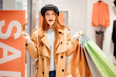 Kafkasyalı neşeli kadın elbise mağazasında indirim kartı tutuyor.