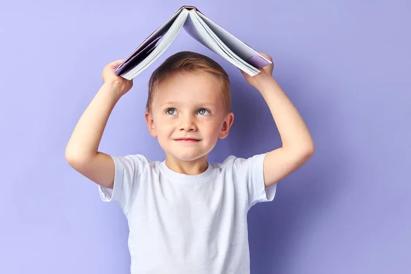 Улыбающийся мальчик с книгой над головой — стоковое фото