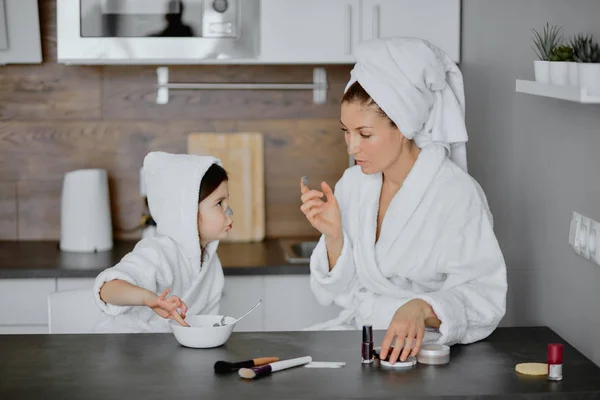 Admirable mujer y niño en toallas y albornoces utilizar máscaras de belleza —  Fotos de Stock