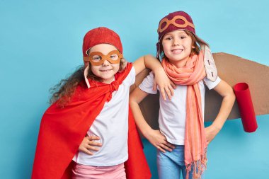 Mavi arka planda pelerin giyen oyuncak uçaktaki mutlu çocuklar.