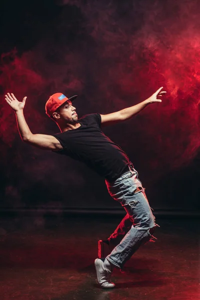 Dancing pose of young man on the dark red smoky background — Stock Photo, Image