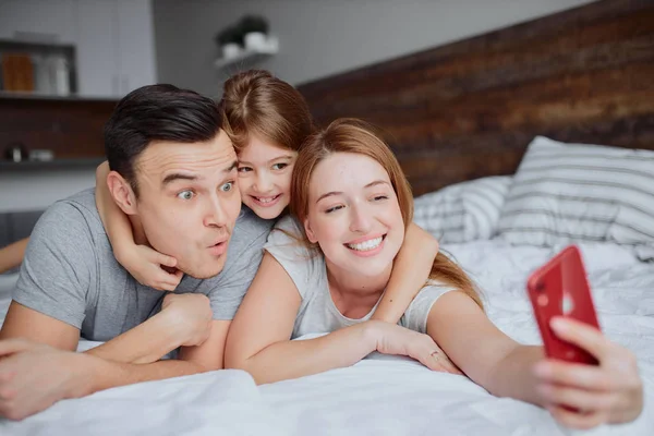 Счастливая улыбающаяся семья делает селфи на кровати — стоковое фото