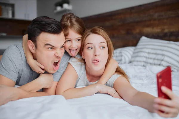 Gelukkig glimlachen familie nemen selfie op bed — Stockfoto