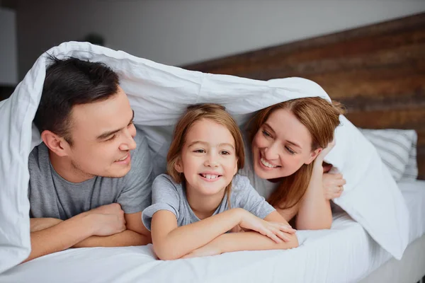 Portrait de parents souriants et fille au lit — Photo