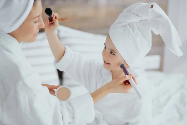 Půvabná holčička aplikující make-up štětcem na matku — Stock fotografie