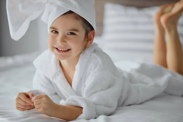 Chica hermosa caucásica en albornoz y toalla acostado en la cama y sonrisa —  Fotos de Stock