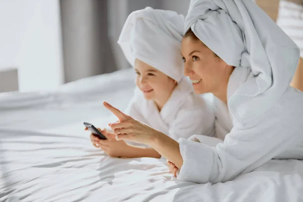 Retrato de madre e hija encantadora en la cama con control remoto de televisión —  Fotos de Stock
