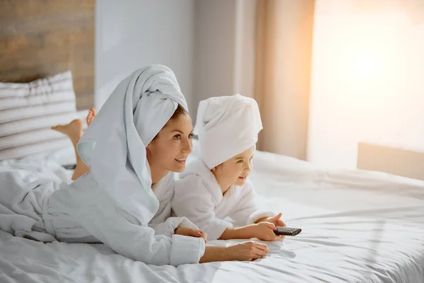 Retrato de madre e hija encantadora en la cama con control remoto de televisión —  Fotos de Stock