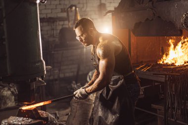 Güçlü kaslı demirci demiri ateşe hazırlar.