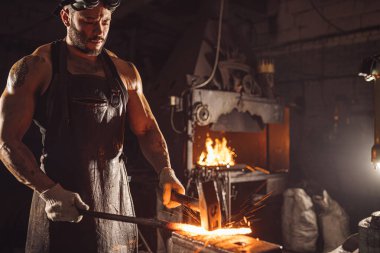 Genç sakallı demirci metali ısıtıyor.