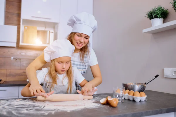 caucasian woman teaching daughter how to roll the dough