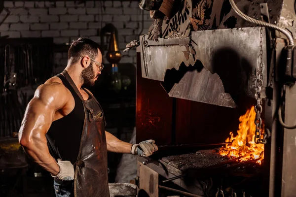 Trabajador metalúrgico joven caucásico trabajando con metal calentado en taller — Foto de Stock