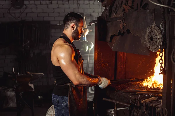 Jovem ferreiro caucasiano, trabalhador de ferro, artesão, mestre artesão em oficina — Fotografia de Stock