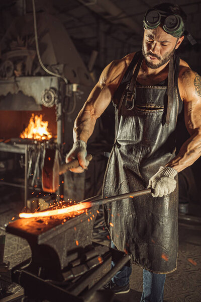 young blacksmith beating iron with hammer