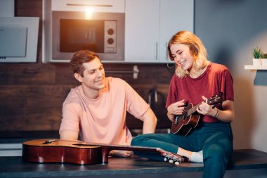 Beyaz tenli kısa saçlı sarışın kadın erkek için ukulele çalıyor.