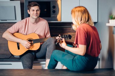 İki pozitif genç arkadaş oturup gitar çalar ve dinlerler.