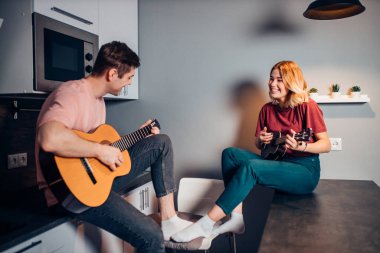Kafkasyalı çift evde gitar ve ukulele çalıyor.