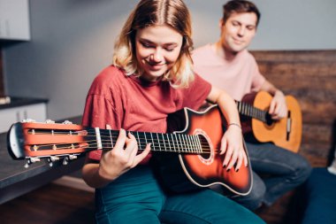 Güzel kız ve yakışıklı adam evde birlikte gitar çalıyorlar.