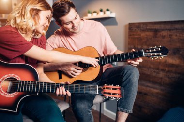 Genç beyaz kadın gitar çalmayı gösteriyor.