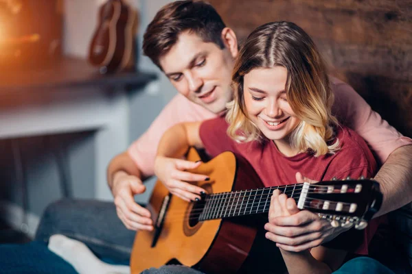 Hermosa chica y chico guapo tocando la guitarra juntos en casa — Foto de Stock