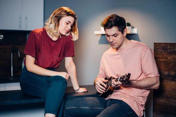 two caucasian friends playing ukulele havaiian instrument at home