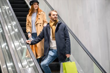 Kafkasyalı genç bir çift ve yürüyen merdivende kese kağıtları.