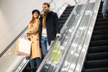 Kafkasyalı güzel bir çift ve yürüyen merdivende kese kağıtları.